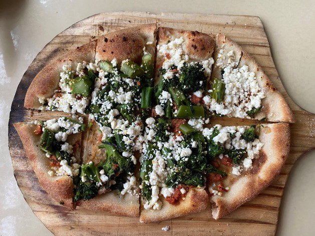 A pizza with cheese and broccoli on a wooden board

Description automatically generated