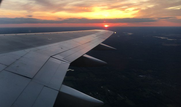 An airplane wing with the sun setting in the background

Description automatically generated