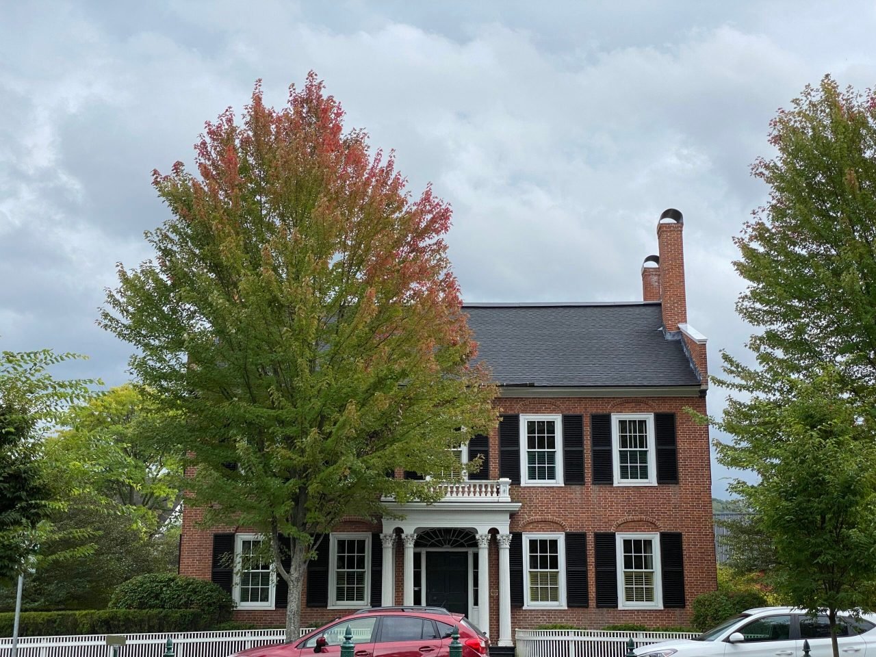 A brick house with trees and a white fence
Description automatically generated