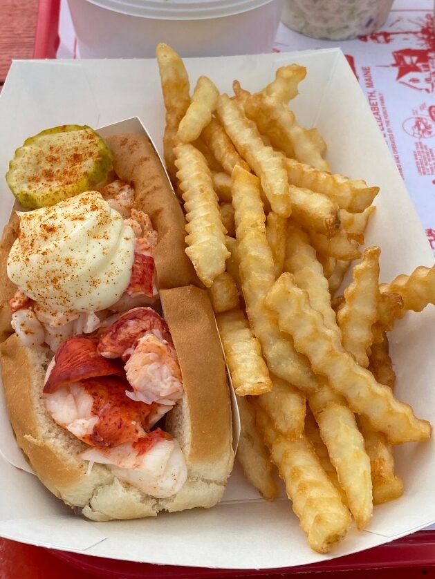 A lobster roll and fries in a white container
Description automatically generated