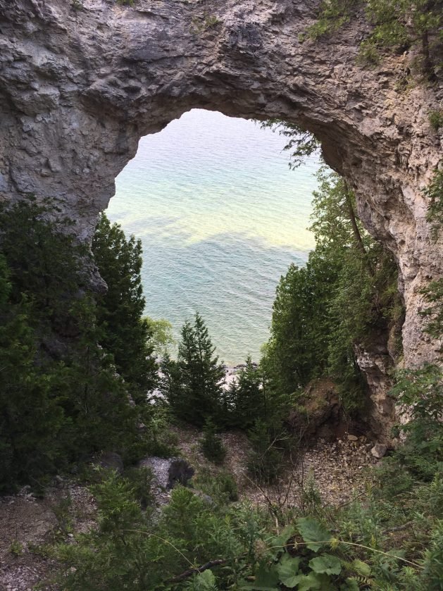 A rock arch with trees and water in the background

Description automatically generated