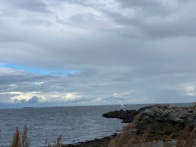 A rocky shore with a sailboat in the distance
Description automatically generated