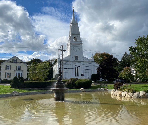 A white building with a fountain in front of it Description automatically generated